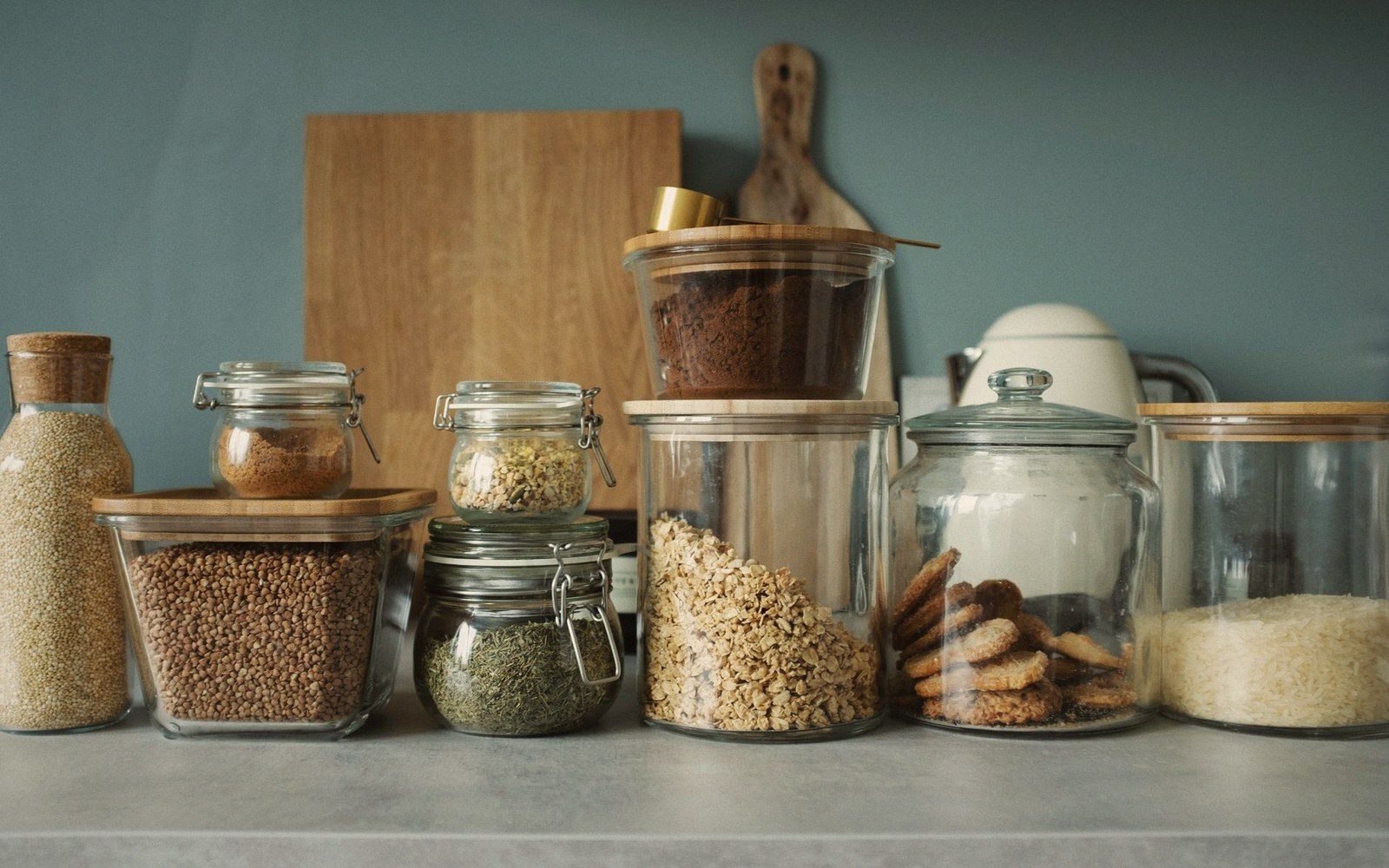 Glass jars of grains, herbs, cookies and rice lined up on a kitchen counter