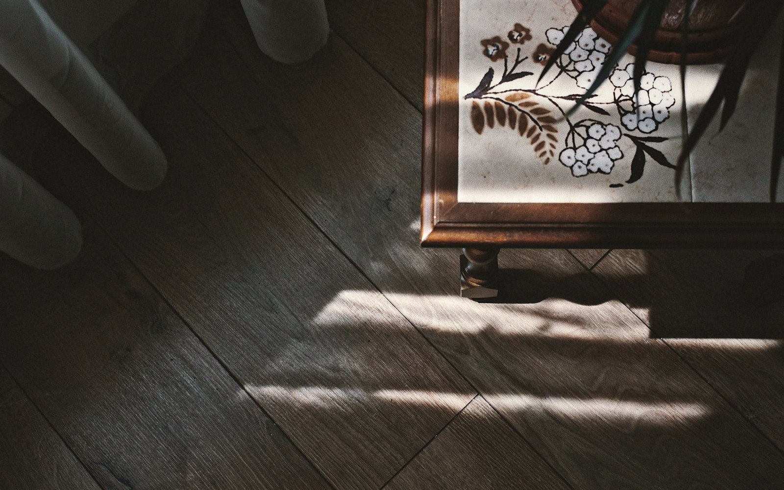 Sunlight streaks across a wooden floor beside a floral-patterned cabinet leg